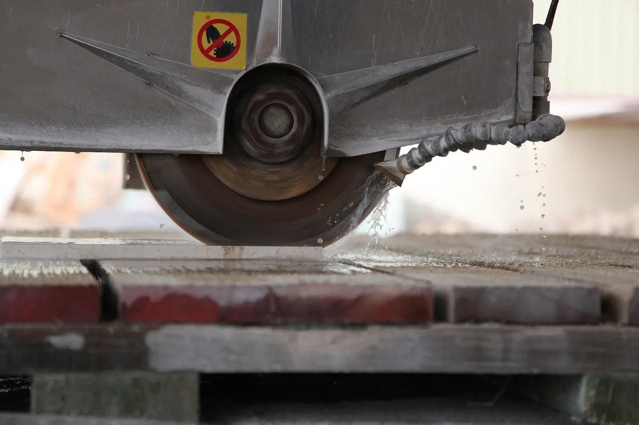 Stationäre Steinsäge mit Diamantsägeblatt unter Schutzhaube schneidet nass durch Steinplatten, Kühlwasser tropft vom Blatt