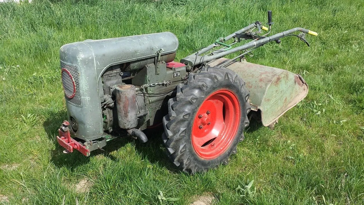 Älterer grauer Einachsschlepper mit roten Felgen, Stollenreifen und angebauter Bodenfräse steht auf einer Wiese