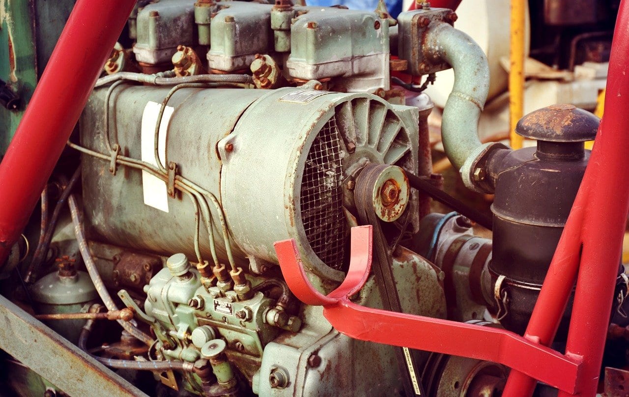 Luftgekühlter Dieselmotor eines alten Schleppers mit Lüfterrad hinter Schutzgitter, Keilriemen und dünnen Einspritzleitungen