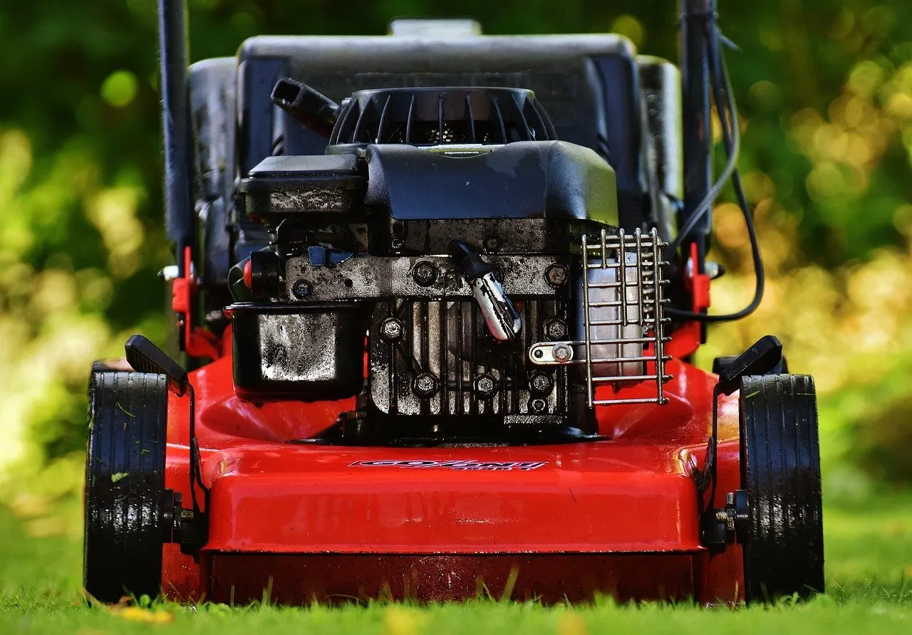 Roter Benzinrasenmäher frontal auf dem Rasen, der Motor mit Kühlrippen, Zündkabel und Luftfilterdeckel ist deutlich verschmutzt